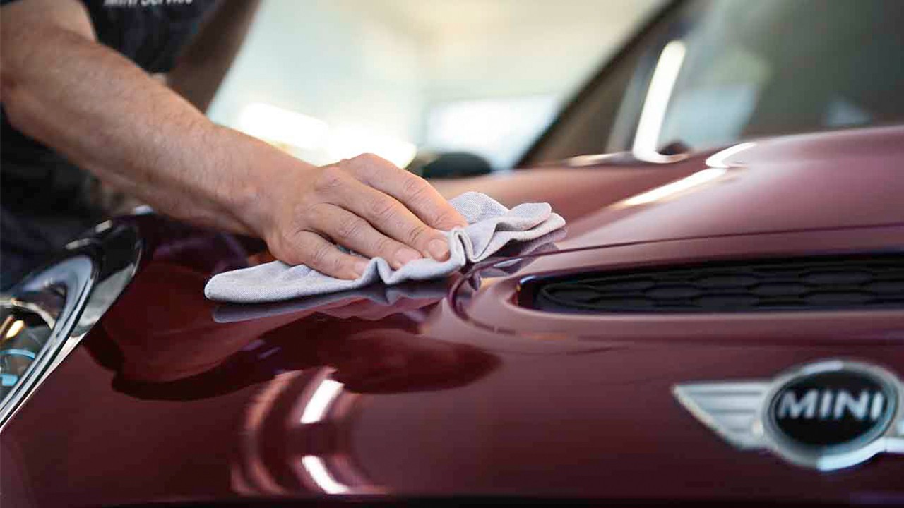 Hand wiping the bonnet of a MINI car with a microfiber cloth.
